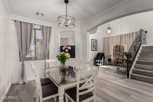 dining space with arched walkways, visible vents, wood finished floors, and ornamental molding