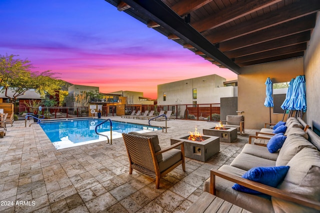 pool at dusk with a patio area and an outdoor living space with a fire pit