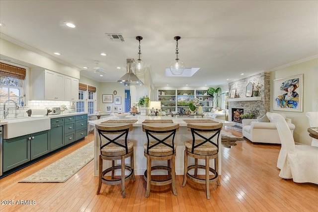 kitchen with white cabinetry, a breakfast bar area, a fireplace, hanging light fixtures, and sink