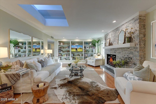 living room with a skylight, a fireplace, built in features, light hardwood / wood-style flooring, and crown molding