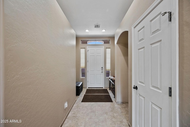 doorway to outside featuring light tile patterned flooring, a textured wall, visible vents, and baseboards