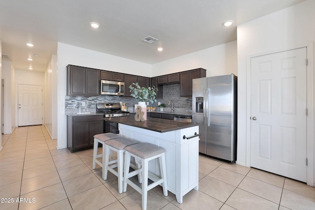 kitchen with dark brown cabinetry, a center island, light tile patterned floors, and stainless steel appliances