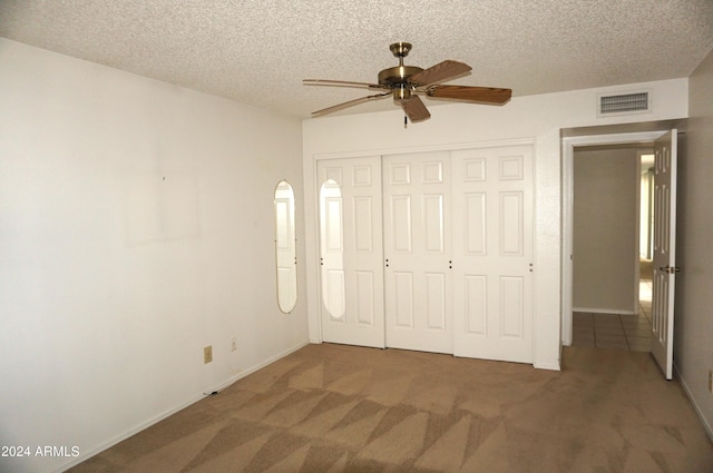 unfurnished bedroom featuring a textured ceiling, a closet, dark carpet, and ceiling fan