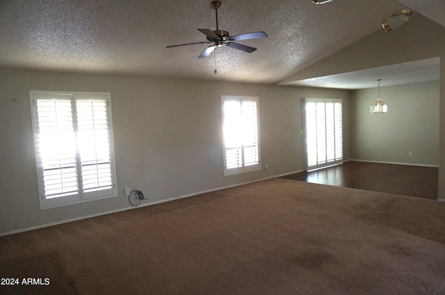 unfurnished room featuring vaulted ceiling, a wealth of natural light, dark carpet, and ceiling fan with notable chandelier