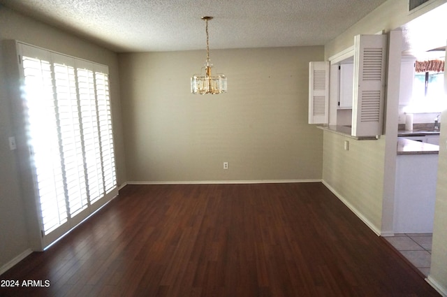 unfurnished dining area featuring sink, dark wood-type flooring, a textured ceiling, and an inviting chandelier