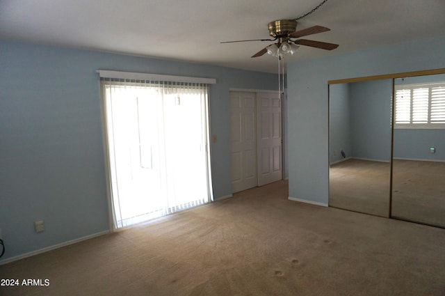 unfurnished bedroom featuring ceiling fan, two closets, light carpet, and multiple windows