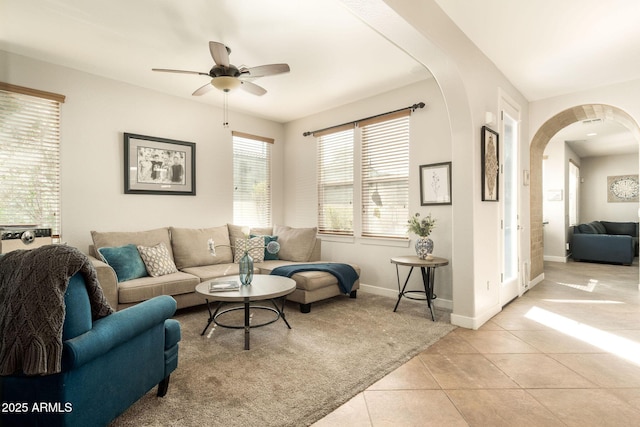 living room featuring arched walkways, a ceiling fan, baseboards, and light tile patterned flooring