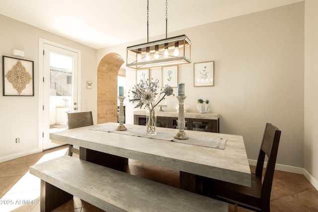 tiled dining area featuring baseboards and arched walkways