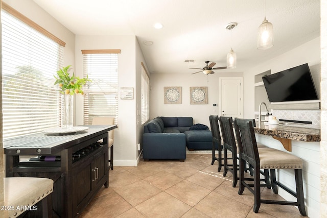 interior space featuring a kitchen bar, a sink, open floor plan, ceiling fan, and hanging light fixtures