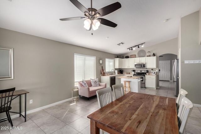 dining space featuring arched walkways, light tile patterned floors, lofted ceiling, visible vents, and baseboards