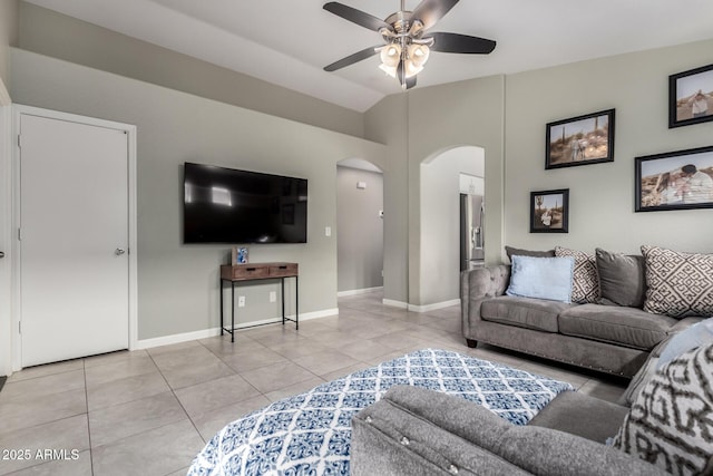 living room featuring arched walkways, light tile patterned flooring, a ceiling fan, baseboards, and vaulted ceiling