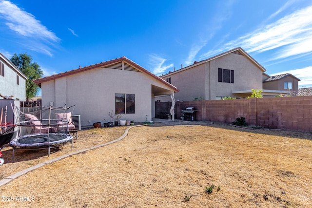 back of house with central air condition unit, a trampoline, fence, and stucco siding