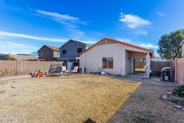 back of house with central AC unit, a fenced backyard, a trampoline, a yard, and stucco siding