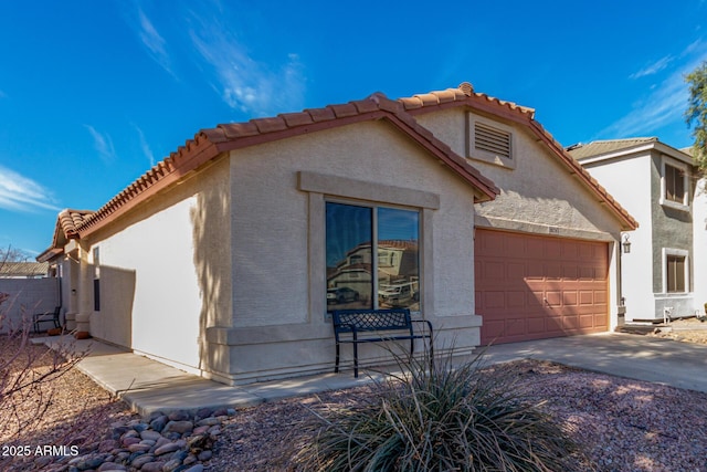 view of property exterior with a tile roof, driveway, an attached garage, and stucco siding