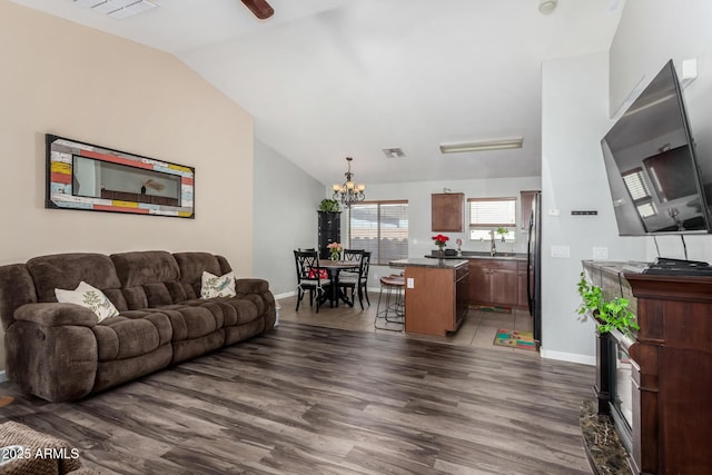 living room featuring ceiling fan with notable chandelier, visible vents, baseboards, vaulted ceiling, and dark wood-style floors