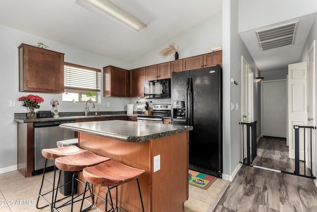 kitchen featuring visible vents, dark countertops, a kitchen breakfast bar, black appliances, and a sink