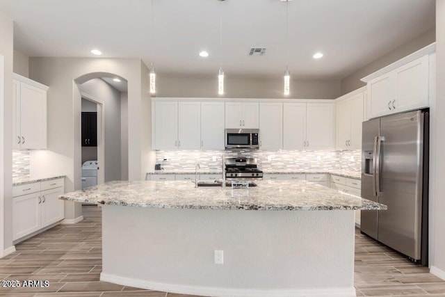 kitchen with pendant lighting, stainless steel appliances, white cabinets, and a center island with sink