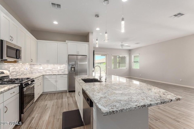 kitchen featuring pendant lighting, white cabinetry, sink, stainless steel appliances, and a center island with sink