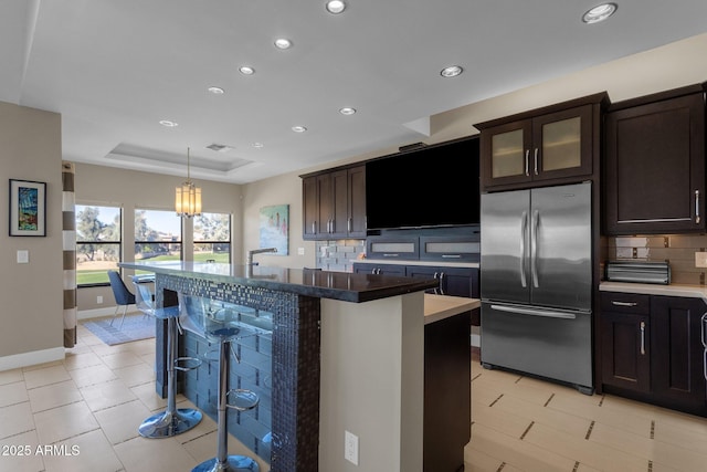 kitchen with a center island, decorative backsplash, a tray ceiling, stainless steel built in fridge, and a breakfast bar area