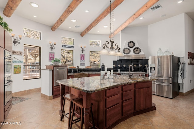 kitchen featuring stone countertops, sink, appliances with stainless steel finishes, beam ceiling, and an island with sink