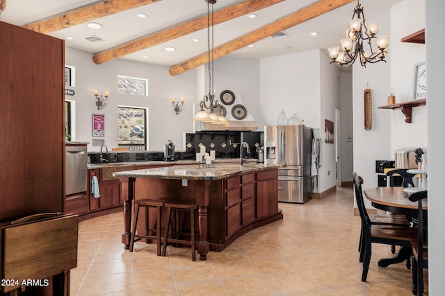 kitchen with pendant lighting, light stone countertops, beamed ceiling, and a kitchen island with sink