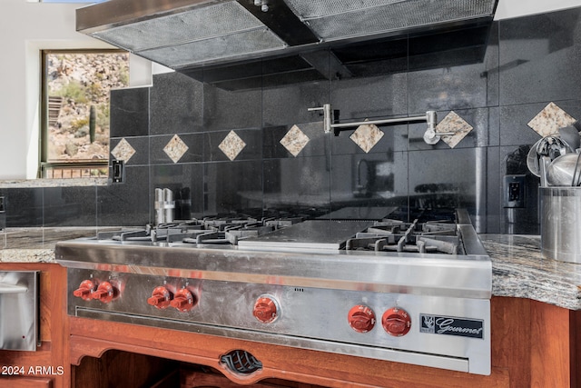 kitchen featuring light stone countertops, stainless steel range with gas stovetop, and backsplash