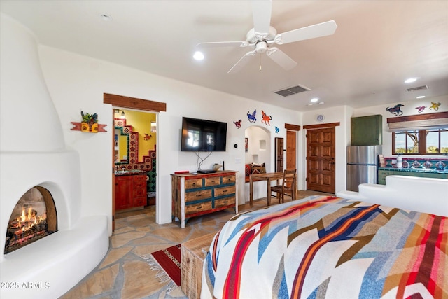 bedroom with ceiling fan, ensuite bathroom, stainless steel fridge, and a large fireplace