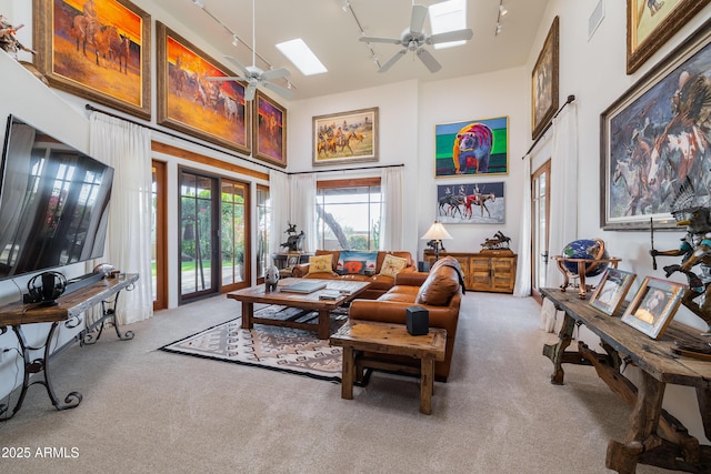 carpeted living room featuring ceiling fan, a towering ceiling, rail lighting, and a skylight