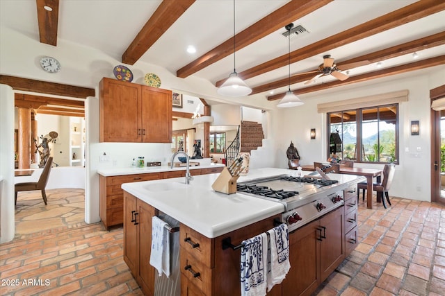 kitchen featuring sink, a kitchen island with sink, hanging light fixtures, stainless steel gas cooktop, and beamed ceiling