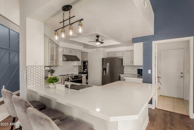 kitchen with a ceiling fan, under cabinet range hood, stainless steel fridge, a peninsula, and light countertops