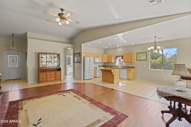 living room with light hardwood / wood-style flooring, ceiling fan with notable chandelier, vaulted ceiling, and sink