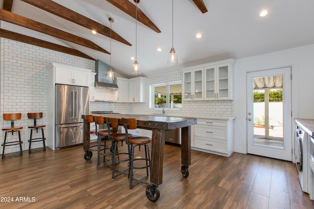 kitchen with high end refrigerator, a kitchen island, white cabinets, wall chimney range hood, and pendant lighting