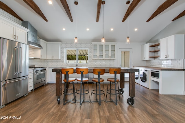 kitchen featuring premium appliances, wall chimney exhaust hood, hanging light fixtures, tasteful backsplash, and white cabinetry