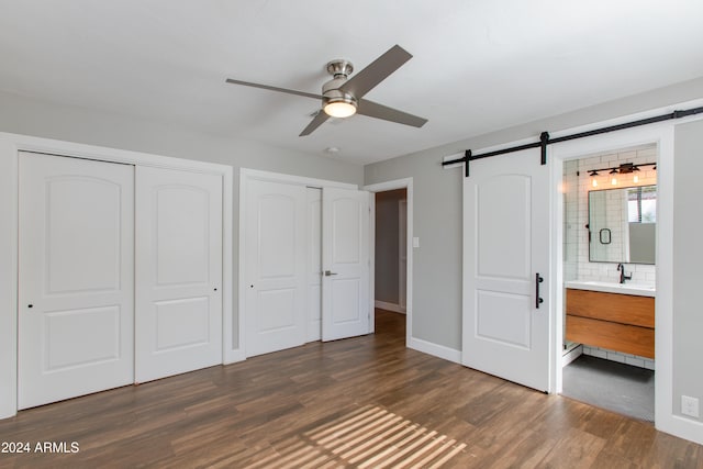 unfurnished bedroom featuring ensuite bath, sink, ceiling fan, a barn door, and dark wood-type flooring