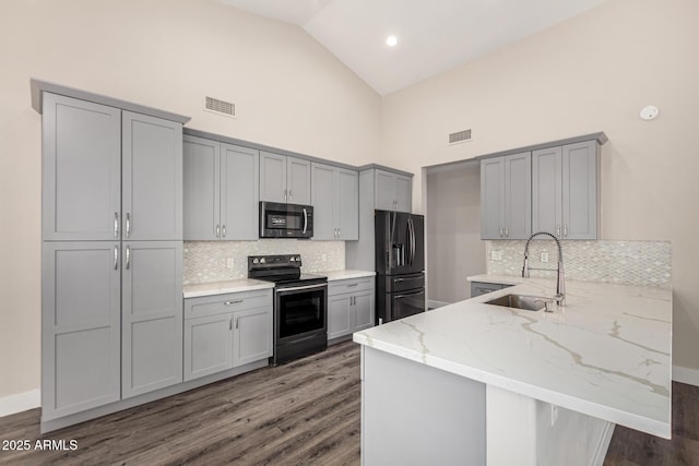 kitchen featuring gray cabinetry, light stone counters, a peninsula, stainless steel appliances, and a sink