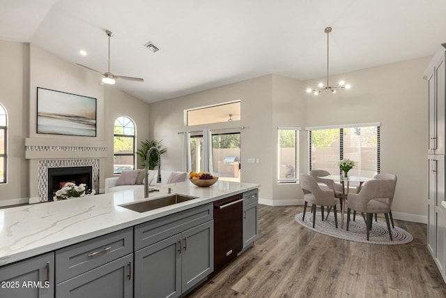 kitchen featuring a tiled fireplace, gray cabinetry, a sink, dishwasher, and open floor plan