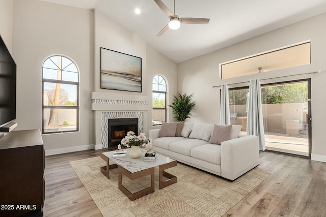 living area featuring a fireplace, wood finished floors, baseboards, and high vaulted ceiling