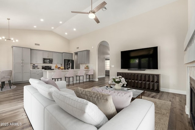 living room featuring high vaulted ceiling, wood finished floors, arched walkways, a fireplace, and baseboards