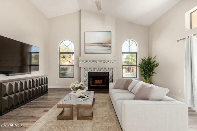 living room with a tiled fireplace, vaulted ceiling, wood finished floors, and baseboards