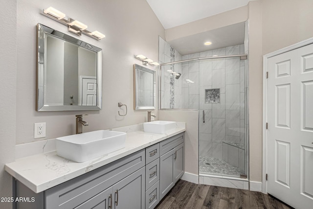 bathroom featuring double vanity, a stall shower, wood finished floors, and a sink