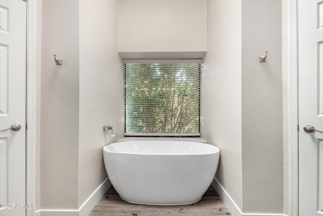 bathroom with a textured wall, a soaking tub, baseboards, and wood finished floors