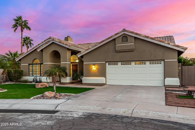 mediterranean / spanish home featuring stucco siding, concrete driveway, a front yard, a garage, and a chimney