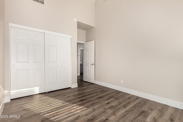 unfurnished bedroom with a closet, baseboards, dark wood finished floors, and a towering ceiling