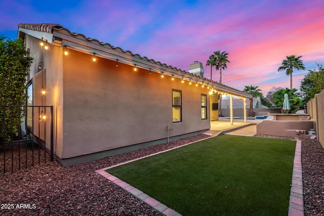 back of property at dusk with stucco siding, a chimney, a yard, a fenced backyard, and a patio area