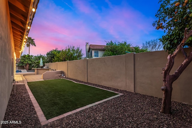 yard at dusk with a patio and a fenced backyard