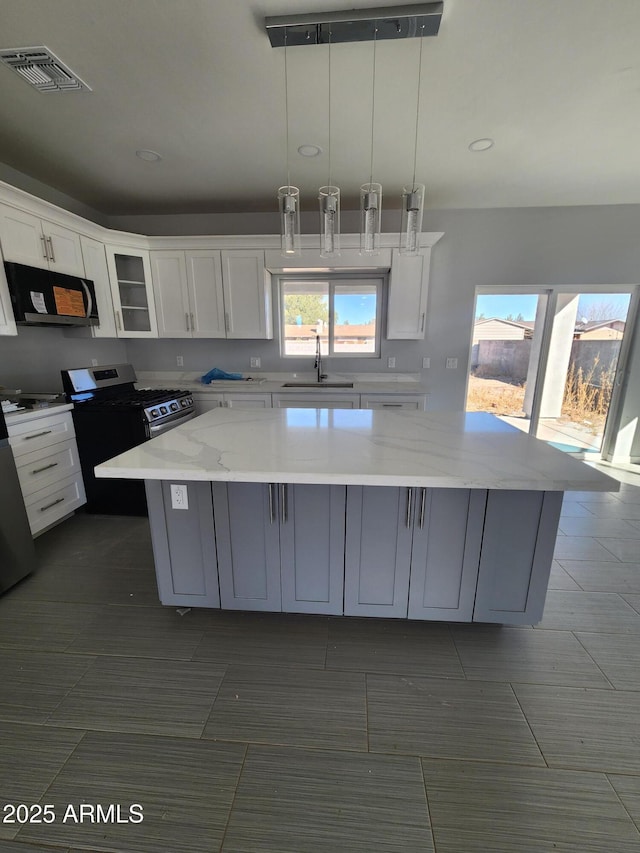 kitchen with pendant lighting, sink, light stone countertops, white cabinets, and a kitchen island