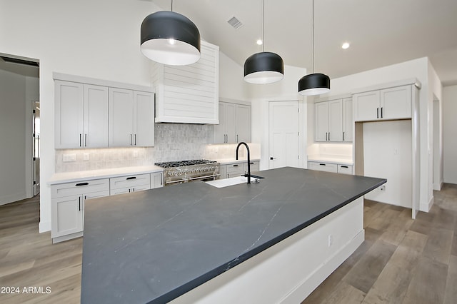 kitchen with a towering ceiling, high end stainless steel range oven, sink, decorative light fixtures, and light hardwood / wood-style floors