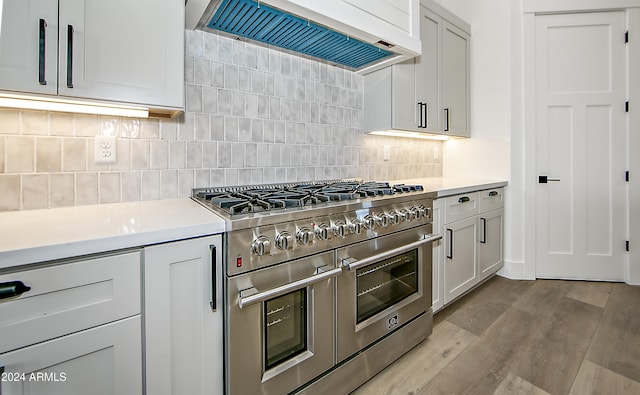 kitchen with backsplash, light hardwood / wood-style floors, double oven range, and premium range hood