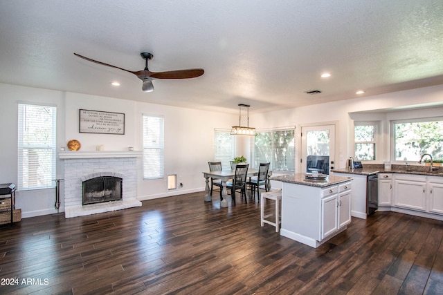 kitchen featuring a kitchen island, decorative light fixtures, a fireplace, dark wood-type flooring, and ceiling fan