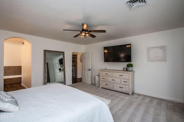 bedroom featuring a textured ceiling, light colored carpet, ensuite bath, and ceiling fan